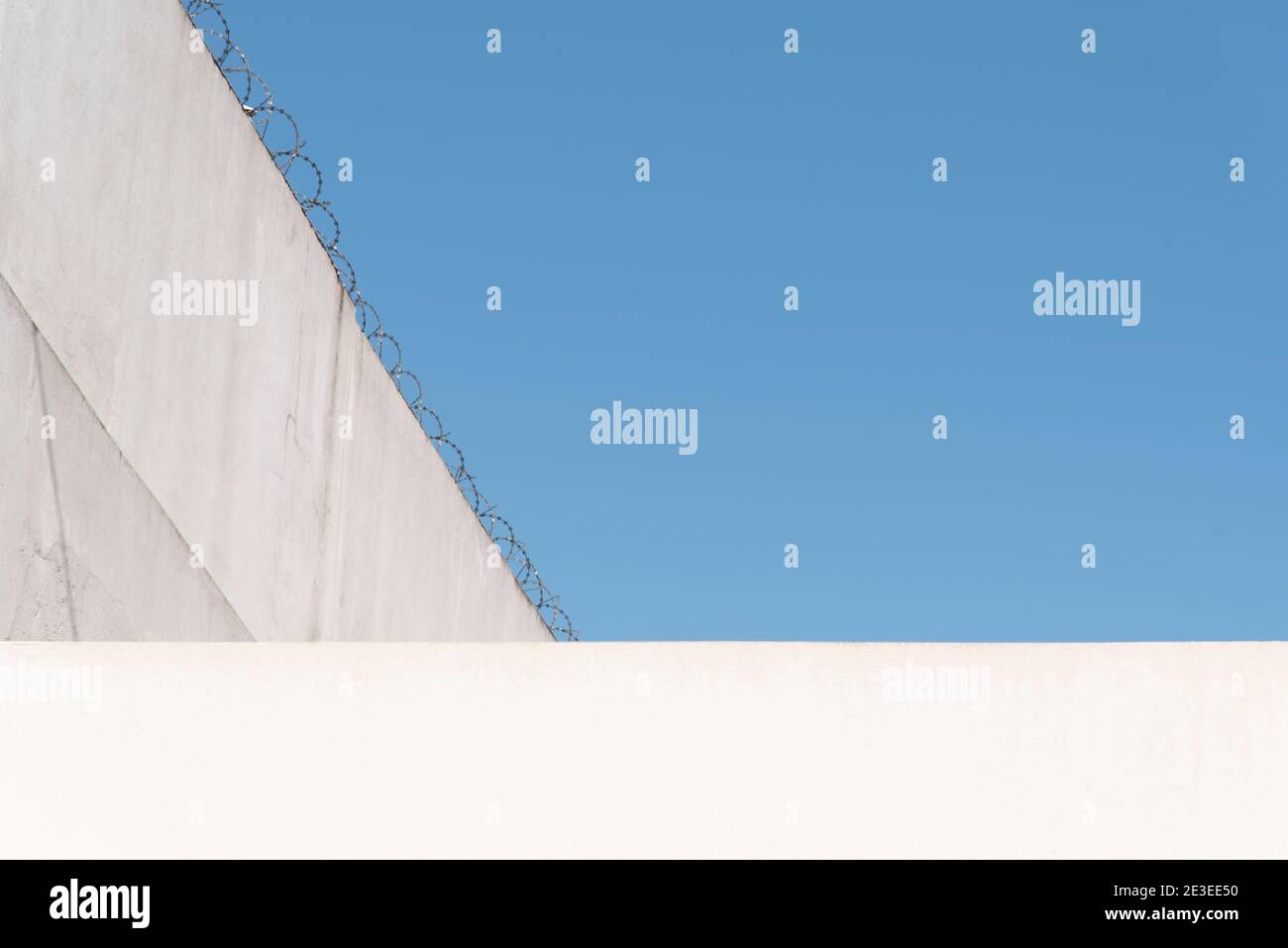 Konzeptuelles Bild, feindliche Architektur der Städte: Wolkenloser Himmel und helle Wände, mit Stacheldraht oben. Geometrisch und hell imag Stockfoto