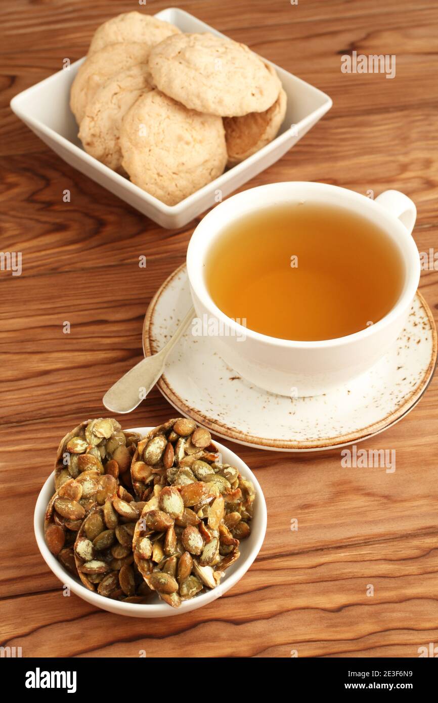 Mandelkekse und mit Zucker überzogene Kürbiskerne Kekse in einer Schüssel und eine Tasse grüner Tee auf einem Holztisch. Nahaufnahme Stockfoto