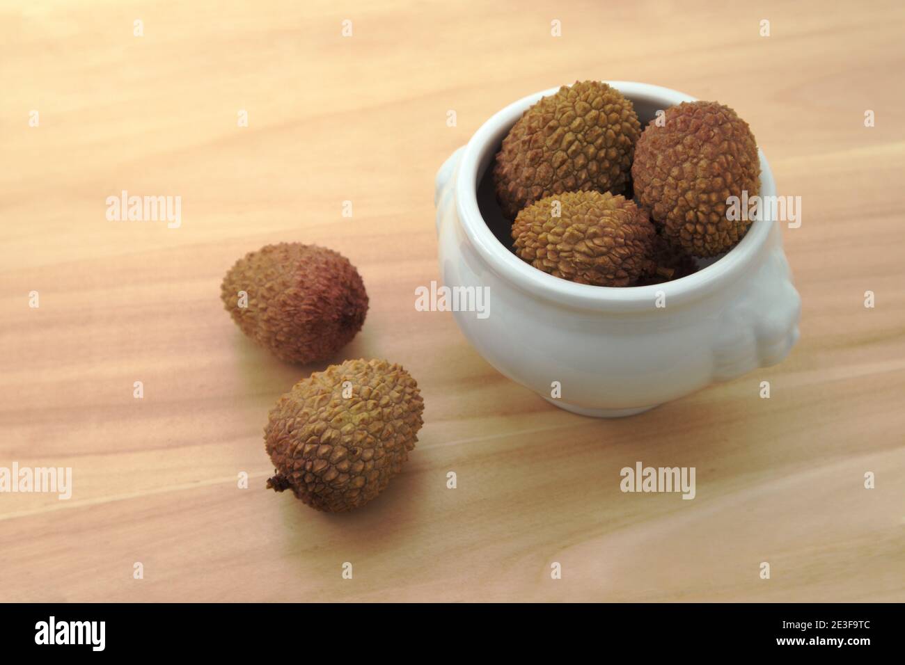 Bild von einigen Litchis (Litchi chinensis) In einer Schüssel, die auf einem Holztisch steht Stockfoto