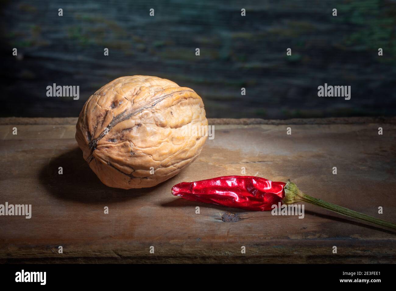 Nussbaum mit getrocknetem Pfeffer auf dem Hintergrund. Makrofoto auf verfallener Holzwerkstoff. Dunkles, Buntes, Unscharfes Holz. Stockfoto