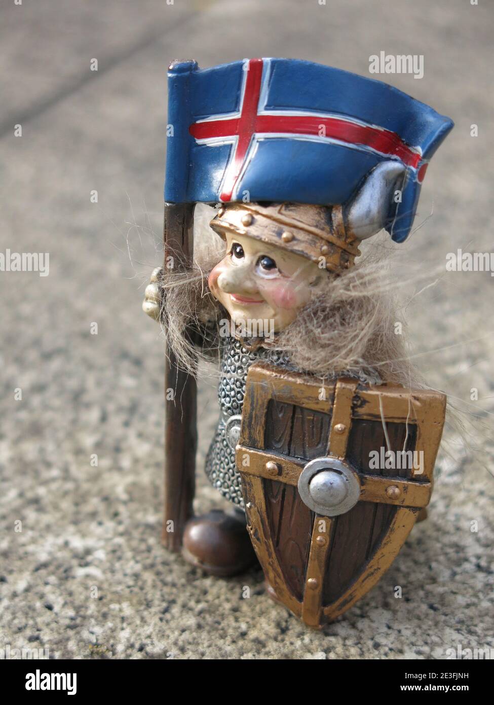 Geschichte Islands: Eine kleine Wikingerfigur, die die isländische Flagge trägt und eine Tunika, einen Helm und einen Schild trägt. Stockfoto