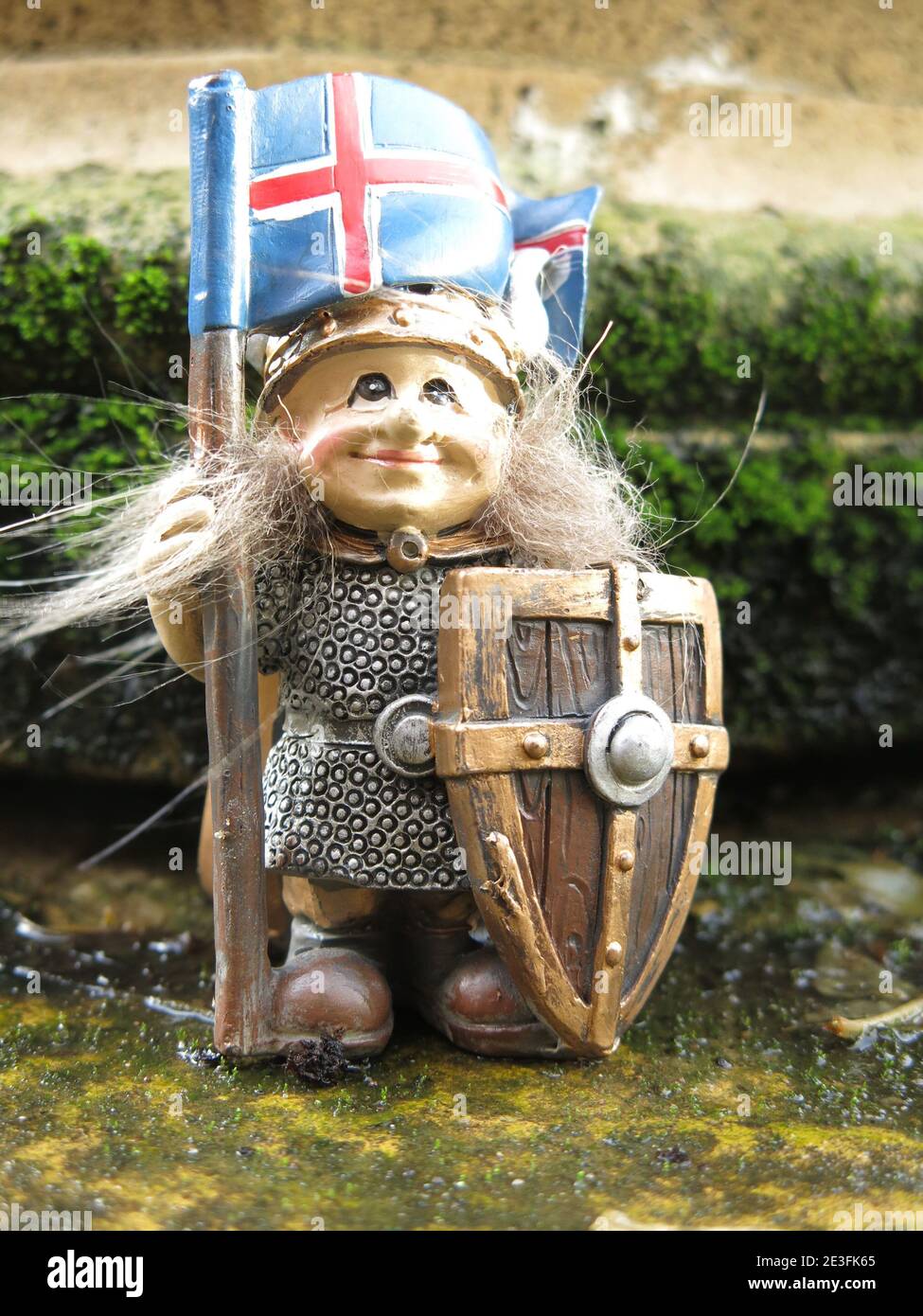 Geschichte Islands: Eine kleine Wikingerfigur, die die isländische Flagge trägt und eine Tunika, einen Helm und einen Schild trägt. Stockfoto