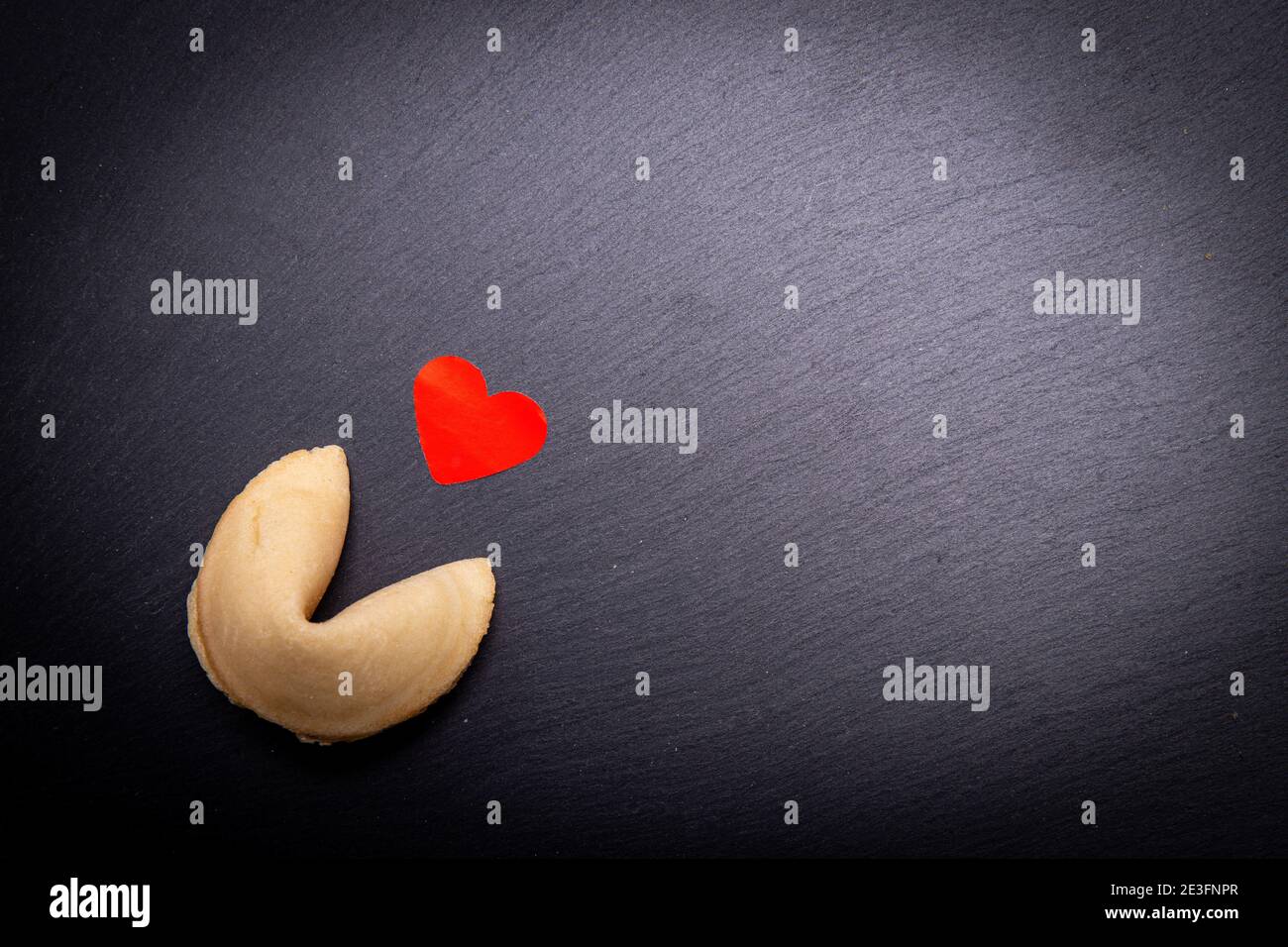 Ein Glückskeks mit einem kleinen roten Herzen auf schwarzem Steingrund. Sind Sie bereit, das Cookie zu brechen und entdecken Sie Ihre Liebe Schicksal? Stockfoto