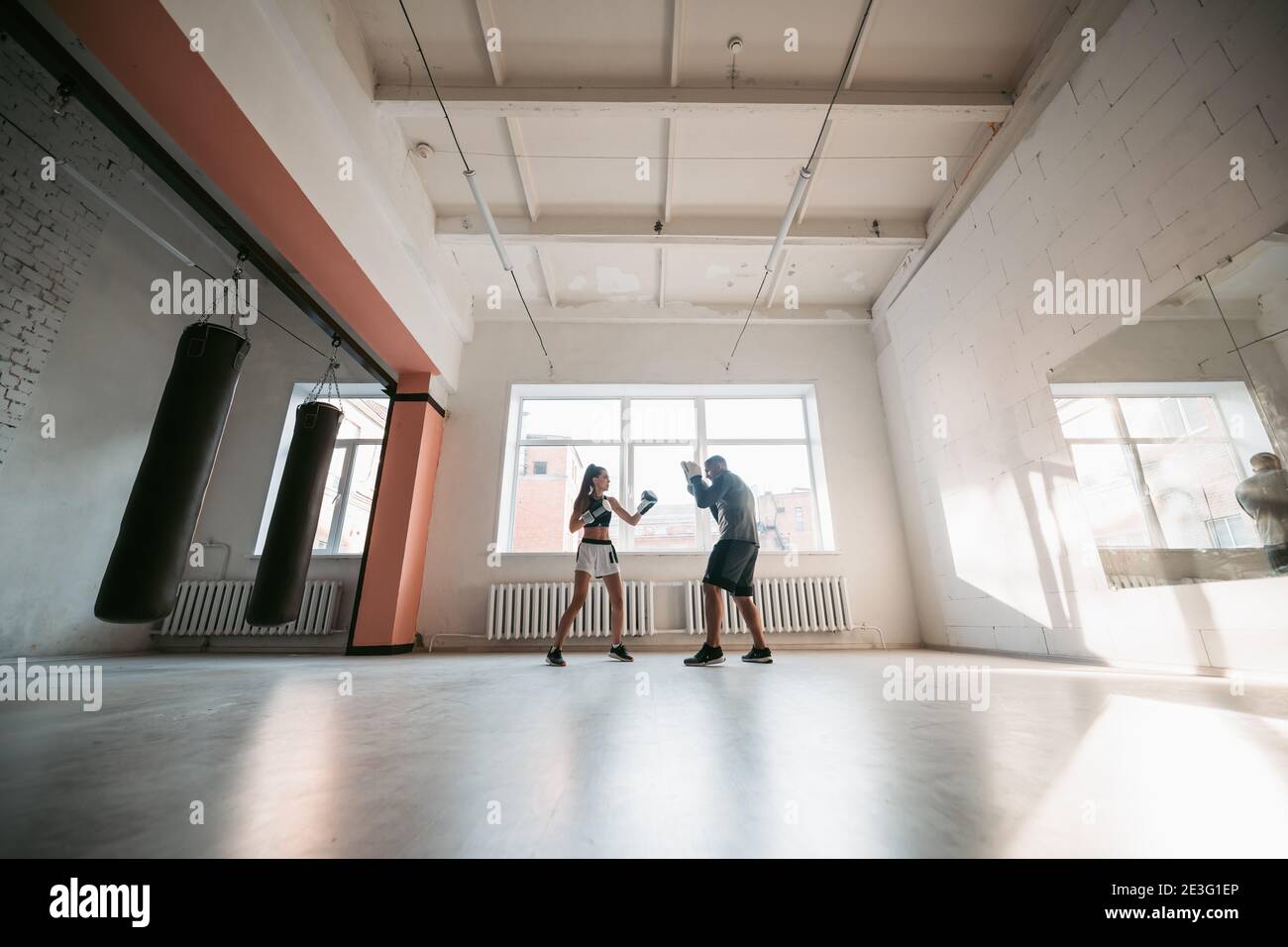 Eine junge Sportlerin in guter körperlicher Verfassung führt Kickboxen durch Training unter der Aufsicht eines erfahrenen Trainers Stockfoto