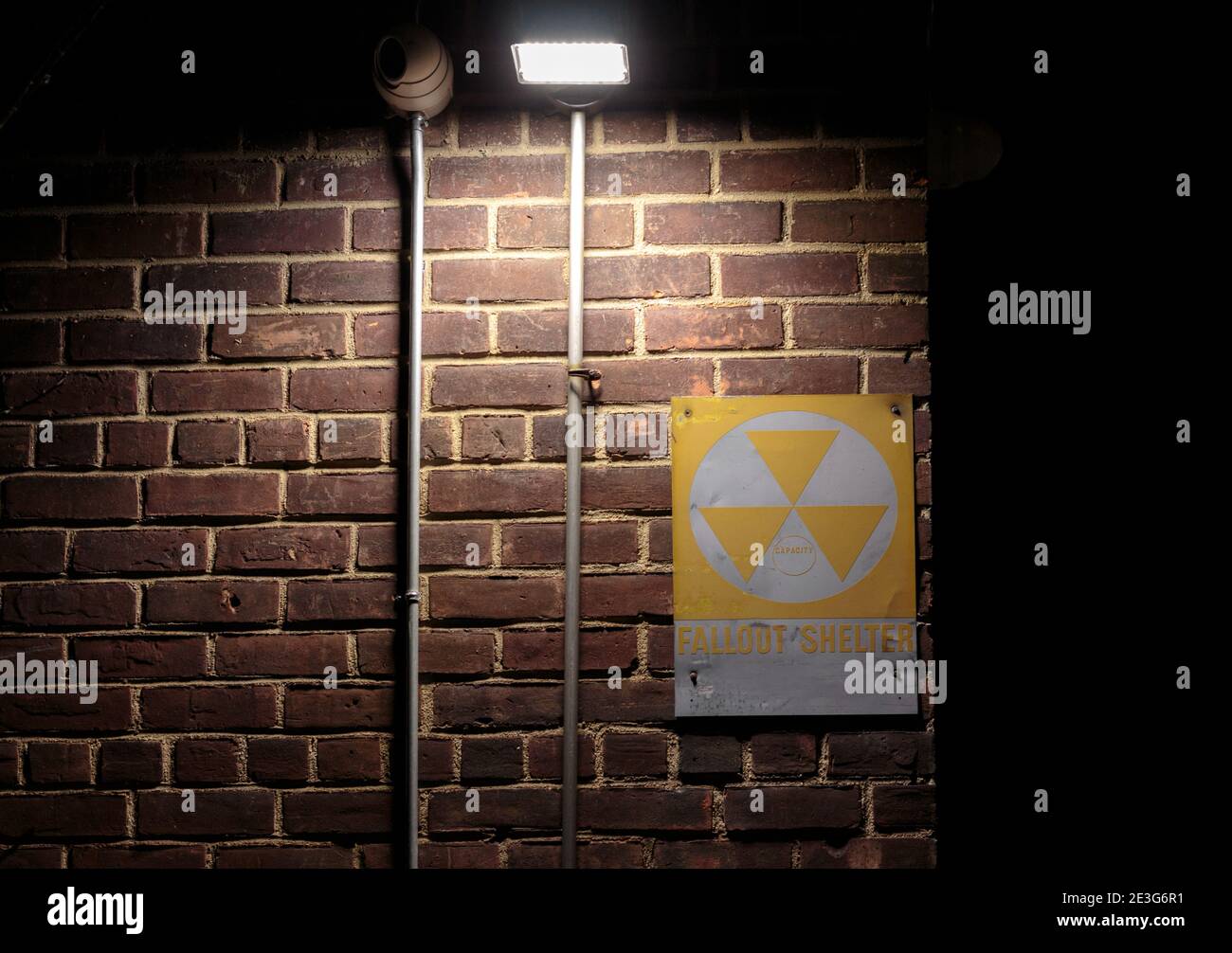 Gelb und weiß Fallout Schutzschild auf einer Mauer in der Nacht mit einem Scheinwerfer leuchtet auf sie Schaffung einer gruseligen, gruselige Szene evozierend Gefahr Stockfoto