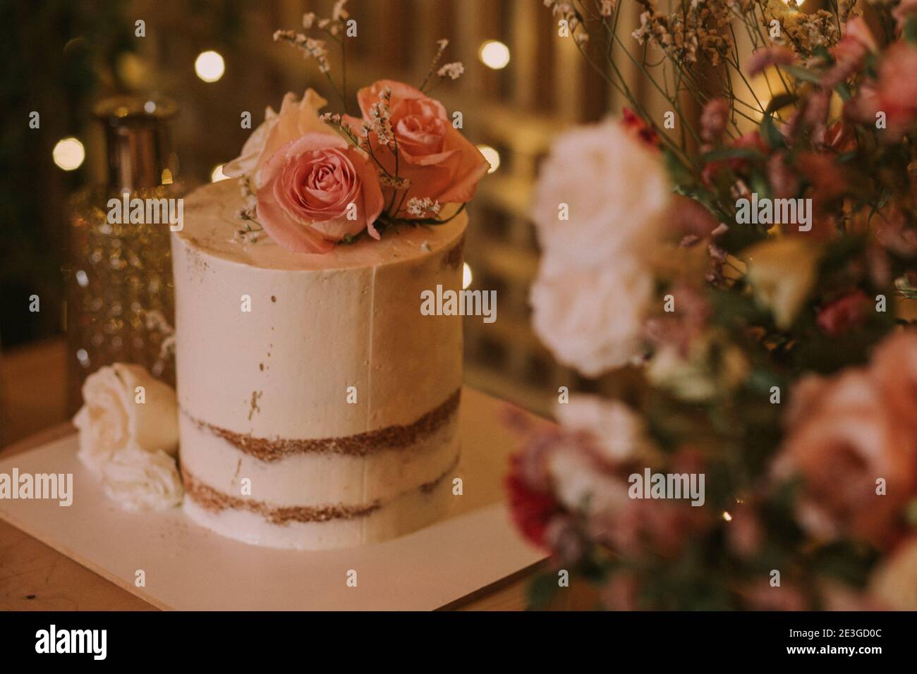 Hochzeitstorte mit rosa Blumen auf einem Holztisch mit Hintergrundbeleuchtung dekoriert. Stockfoto