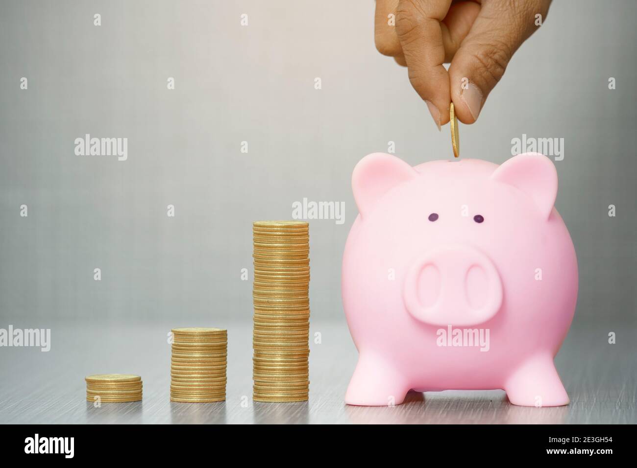 Hand setzen Goldmünze auf Sparschwein auf grauem Hintergrund. Mit Copy Space.Saving Investitionskonzept Stockfoto