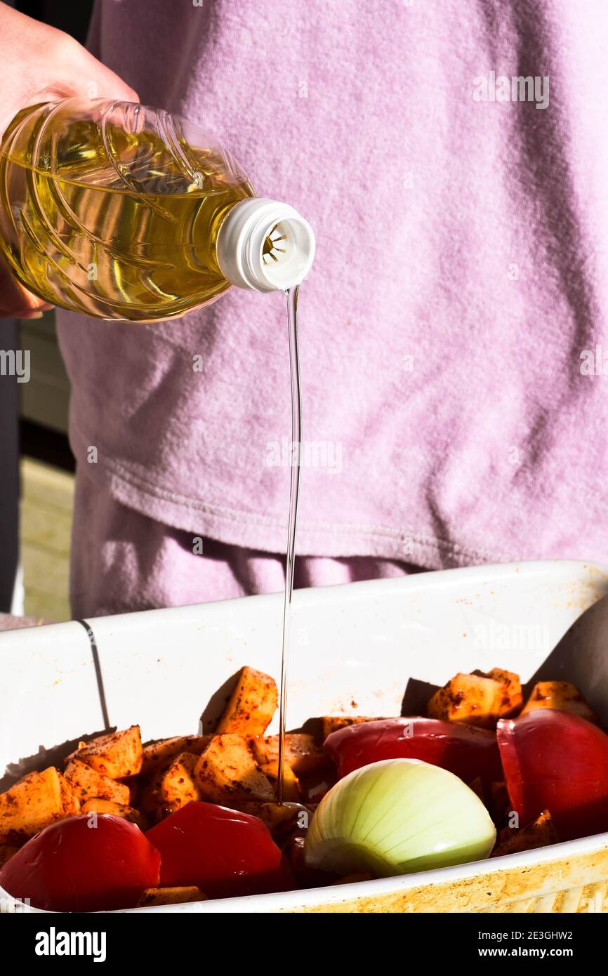 Koch gießt Speiseöl aus der Flasche über rohe Kartoffeln/Lebensmittel Vorbereitung/ Stockfoto