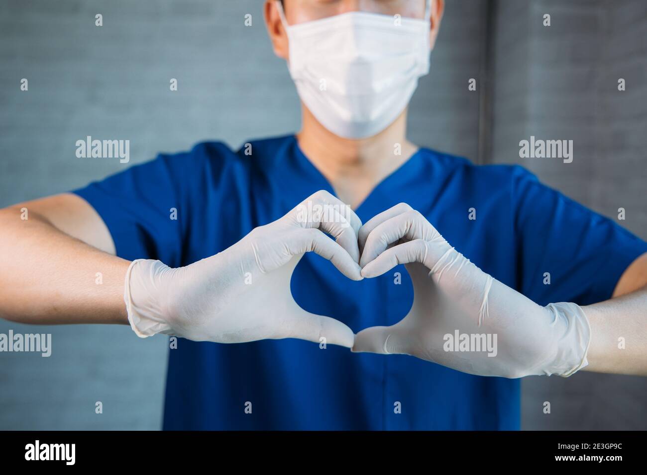 Nahaufnahme des Arztes macht ein Herz Symbol Form Hände Geste mit Kopierraum. Medizinische Arbeiter mit chirurgischen Gesichtsmaske in Peelings zeigen Mitgefühl Stockfoto