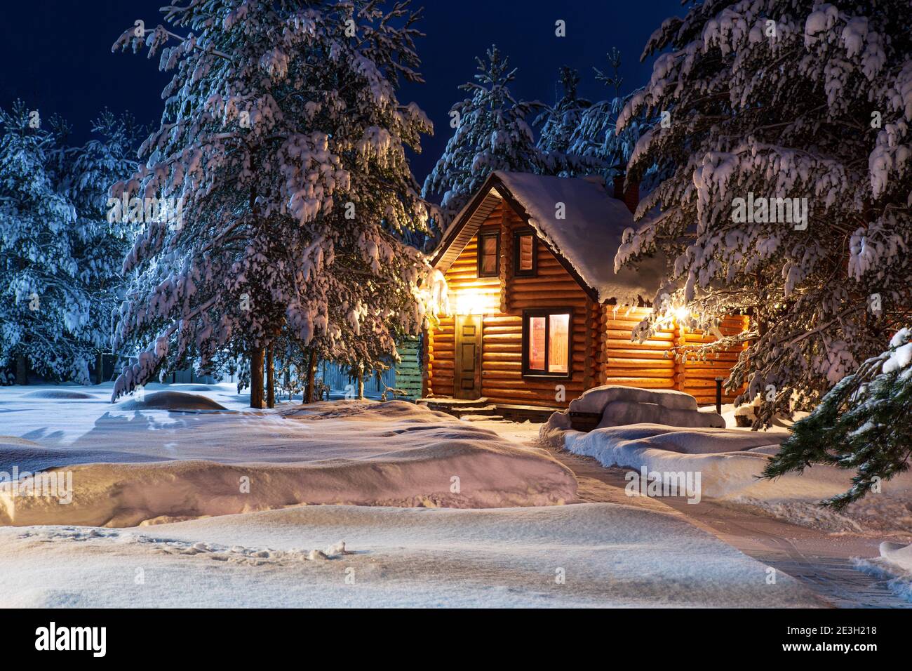 Rustikales Blockhaus, schneebedeckte Pinien, große Schneeverwehungen, fabelhafte Winternacht Stockfoto