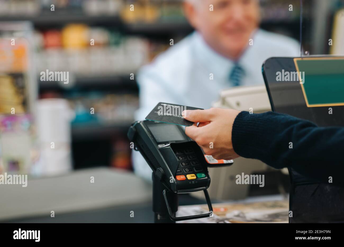 Nahaufnahme eines Kunden zahlt für den Einkauf an einer Supermarktkasse. Kunde, der in einem Geschäft mit einer Kreditkarte bezahlt. Stockfoto