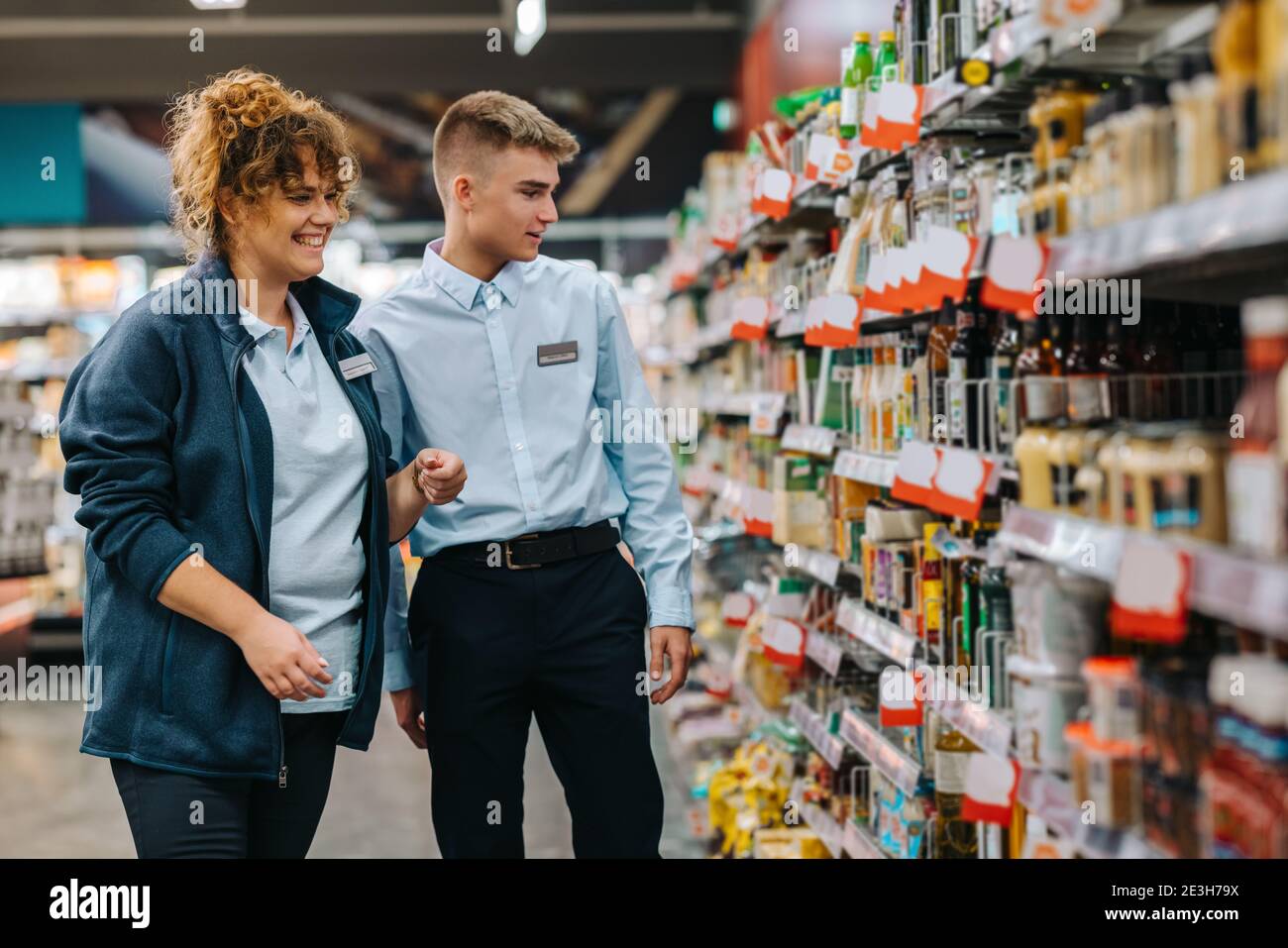 Weibliche Führungskraft hilft neuen männlichen Auszubildenden im Lebensmittelgeschäft. Mann im Urlaub Job bekommen Hilfe vom Manager im Supermarkt. Stockfoto