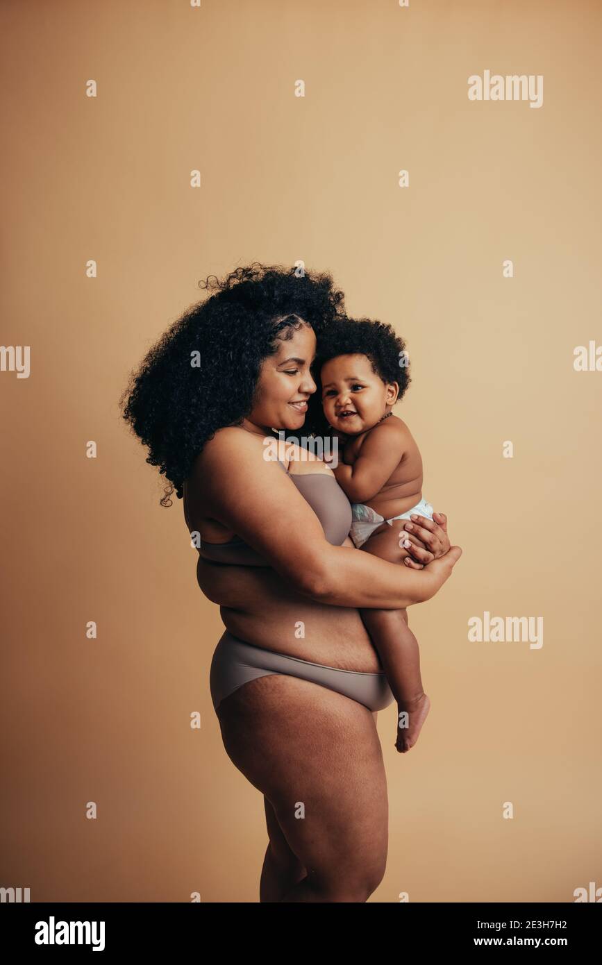 Nettes Baby in den Armen seiner Mutter. Gesunde Frau trägt Baby am Muttertag. Stockfoto