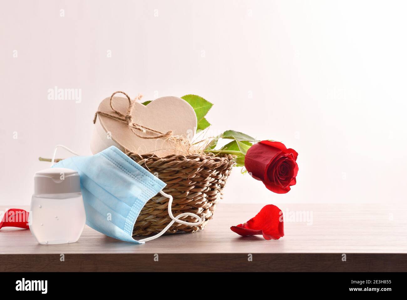 Korbkorb mit Geschenkbox und roter Rose mit Schutz von Masken und Hydro-alkoholische Gel auf Holztisch isoliert weiß. Vorderansicht. Stockfoto