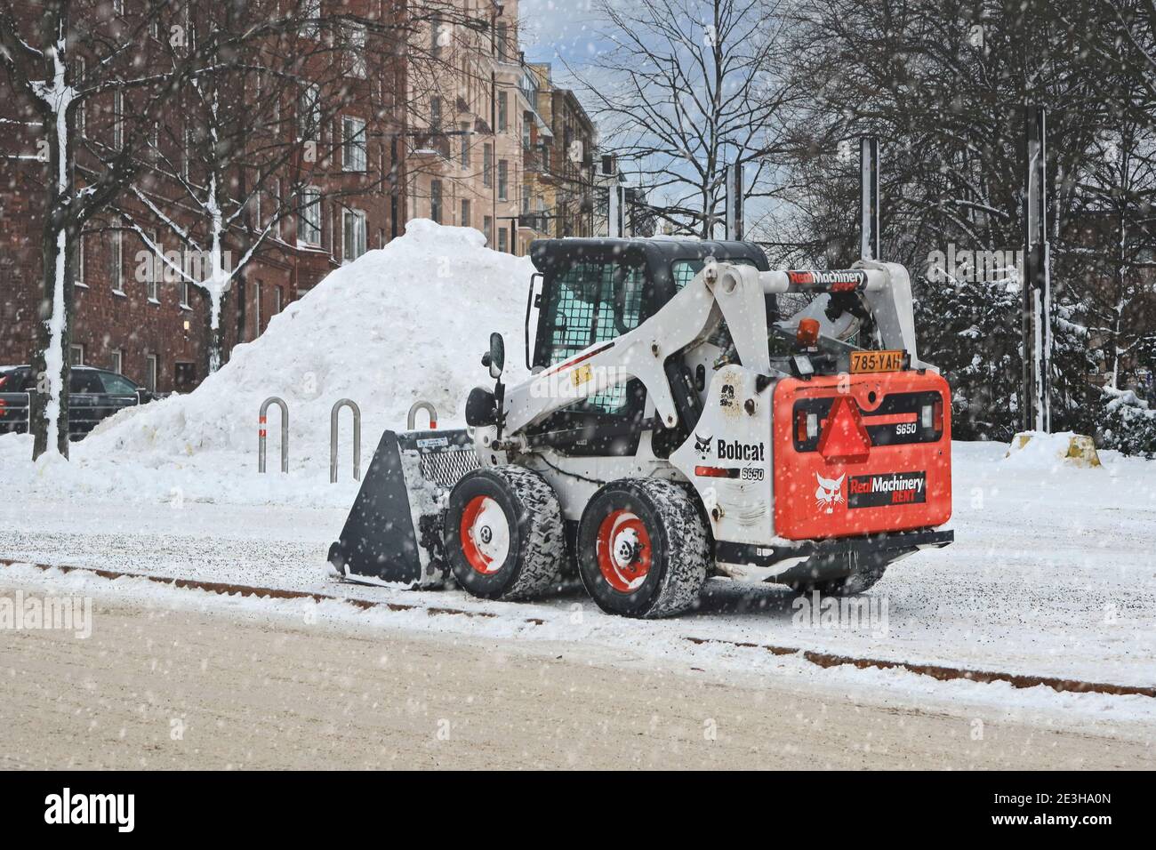 Bobcat S650 Kompaktlader zum Entfernen von Schnee in geparkten am Rande der Stadtstraße, bei leichtem Schneefall. Helsinki, Finnland. Januar 18, 2021. Stockfoto