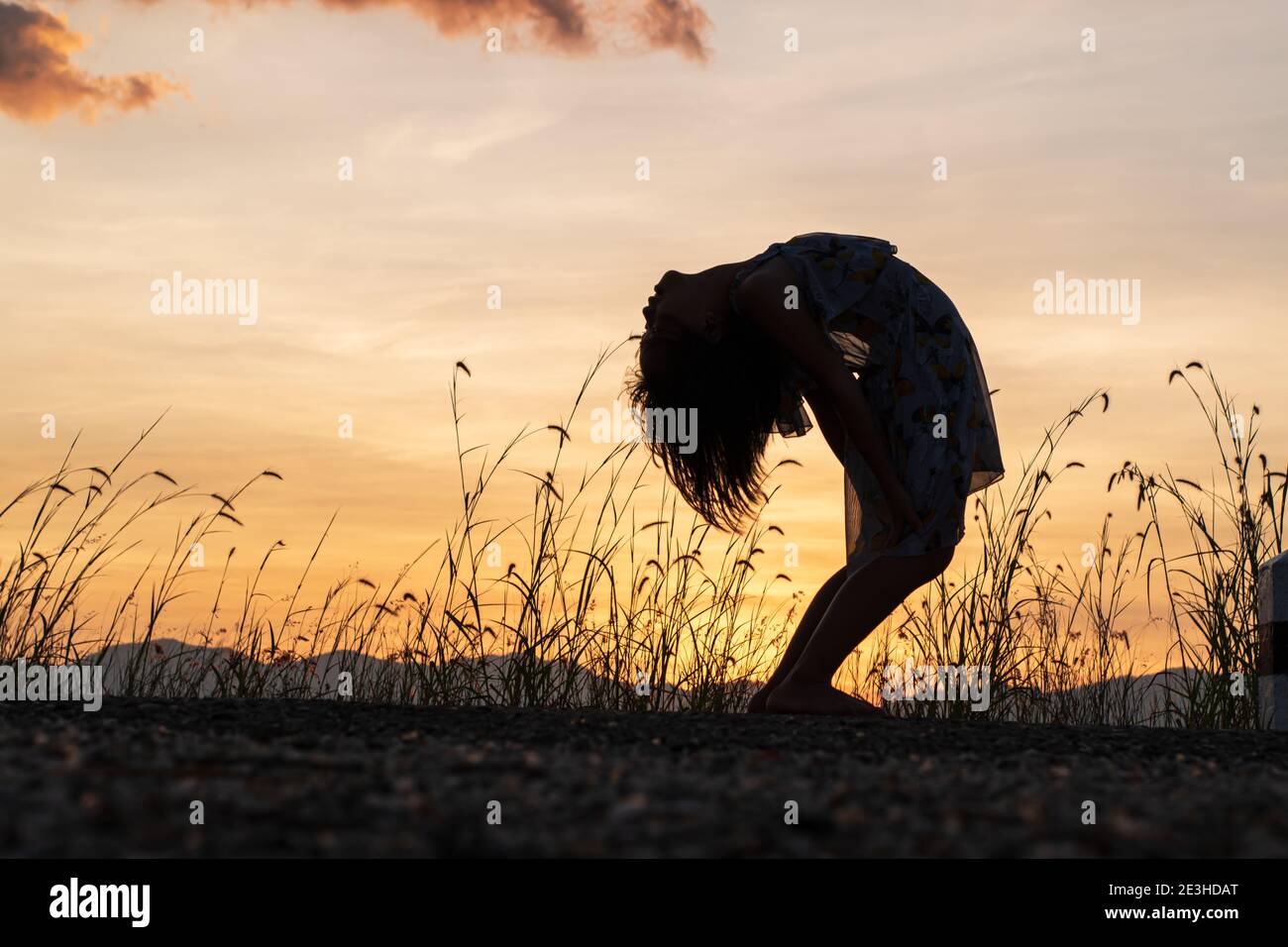 Silhouette des Kindes Mädchen tut Yoga, in Brücke Pose auf Wiese Sonnenuntergang Hintergrund. Sport und Fitness Stretching Training im Freien. Stockfoto