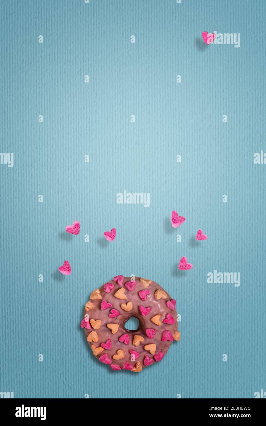 Leckerer rosa Donut mit Marshmallow-Herzen. Nur wenige Herzen fliegen herum. Strukturierter blauer Papierhintergrund. Vorlage für Valentinstag Grußkarte Stockfoto