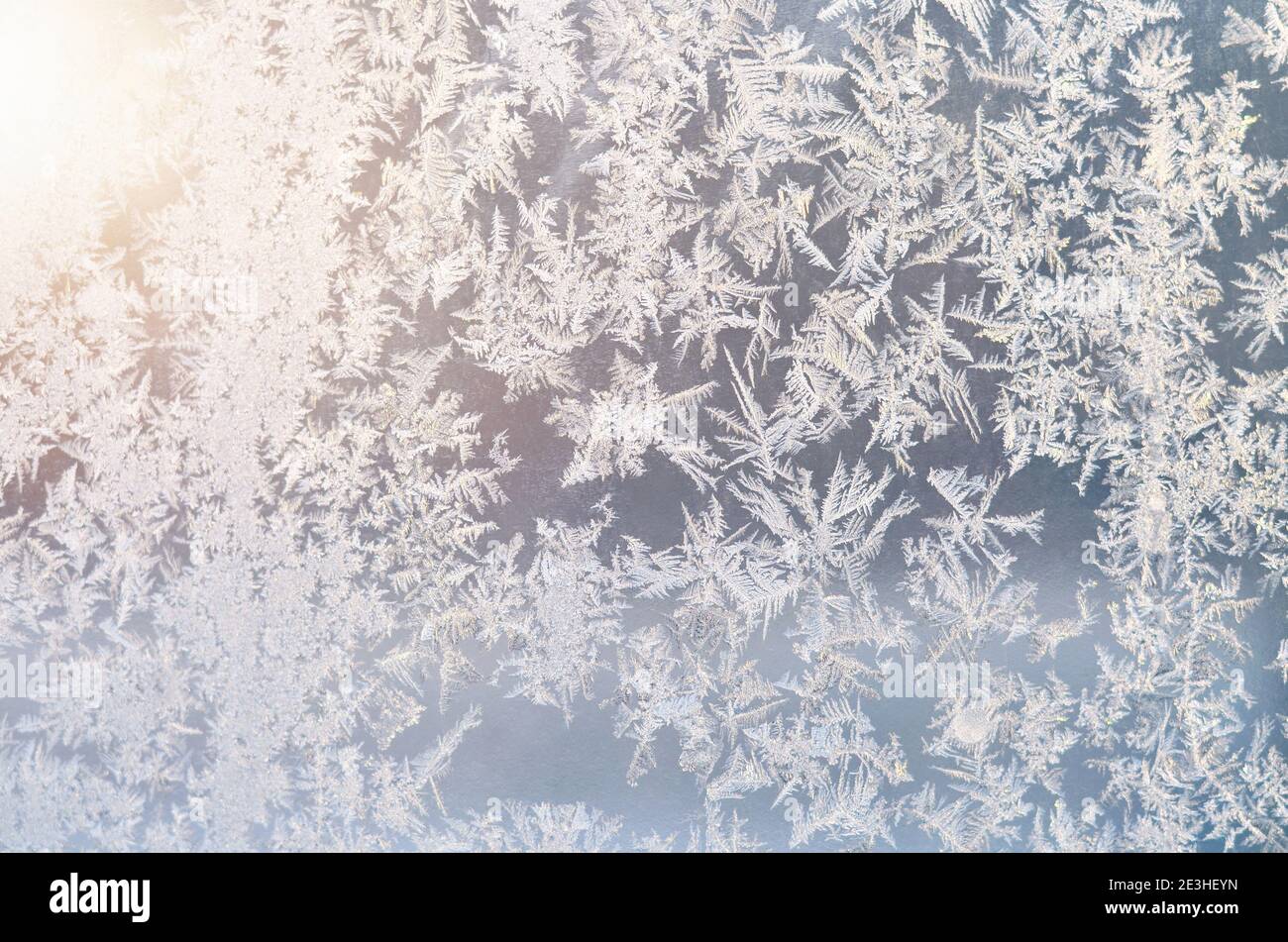 Frostige Muster auf dem von der Sonne beleuchteten Fensterglas Als Winterhintergrund Stockfoto