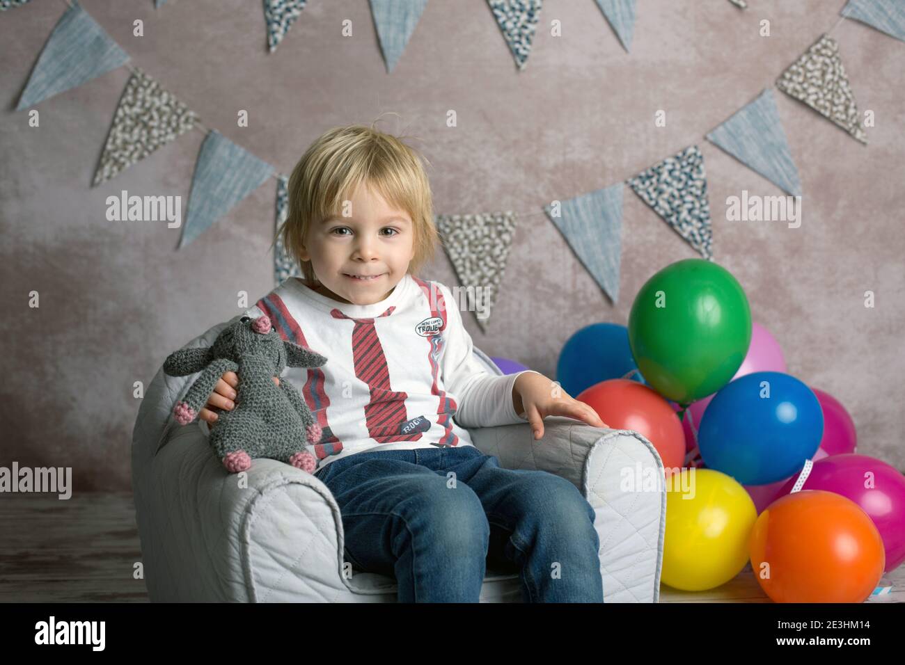 Cute blonde Kleinkind Kind, Junge, sitzen auf kleinen Baby-Sessel, spielen mit bunten Luftballons, glücklich lächelnd, innen erschossen Stockfoto