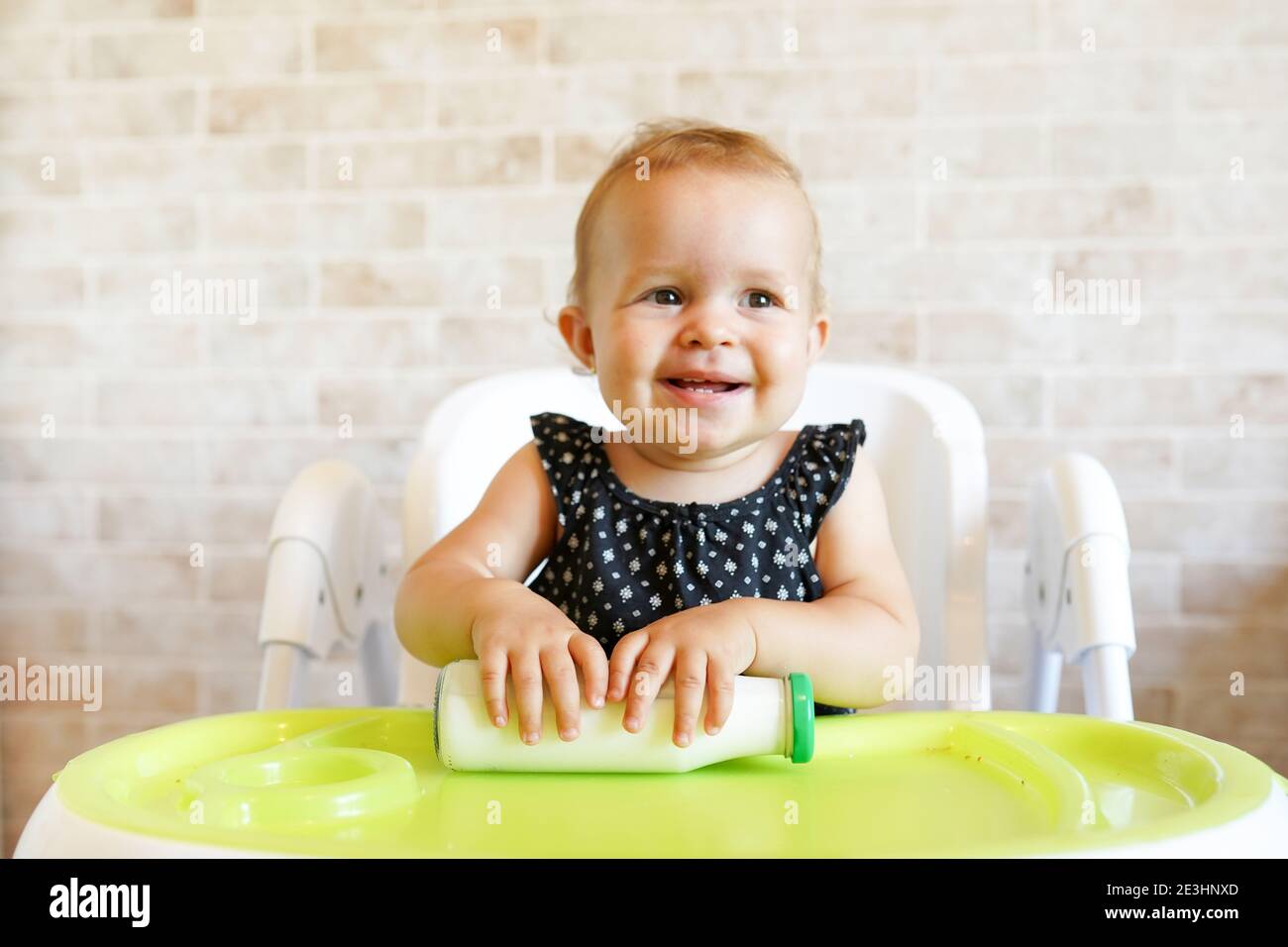 Hübsches Baby Mädchen hält Flasche mit Milch. Kind sitzt auf dem Stuhl zu Hause. Lächelndes Kind ist 7 Monate alt Stockfoto