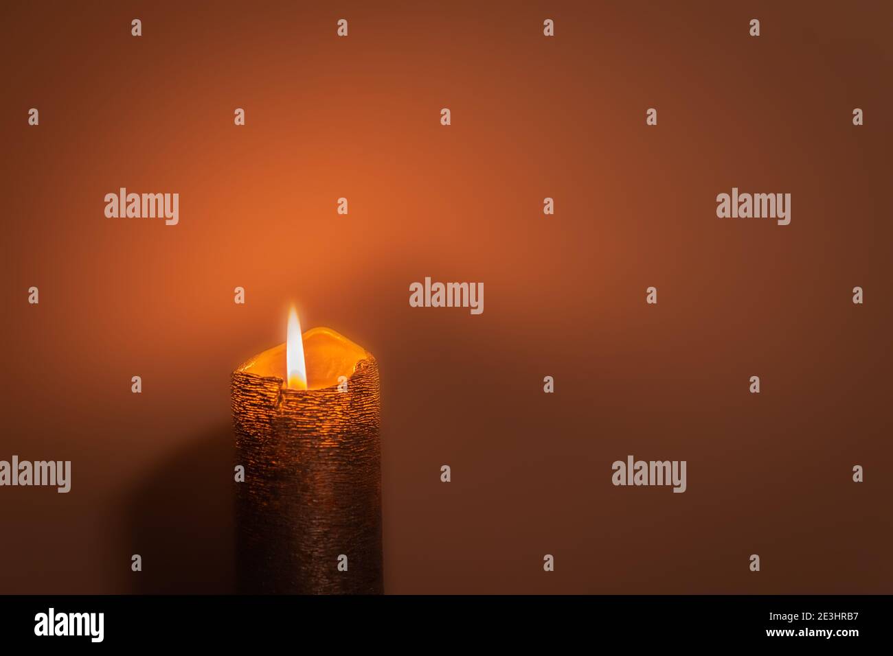 Orange gemusterte brennende Kerze auf dunkelorangenen Hintergrund mit Kopierraum. Kerzenlicht in dunkeloranger Umgebung. Einzelne brennende Kerze Stockfoto