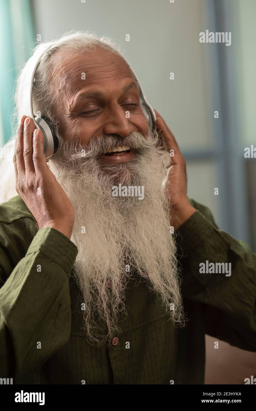 EIN BÄRTIGER ALTER MANN HÖRT GERNE MUSIK AUF KOPFHÖRERN Stockfoto