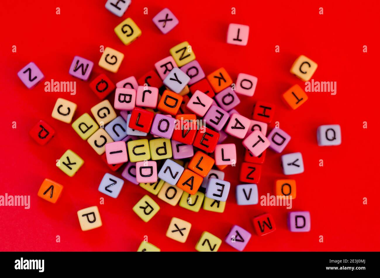 Bunte Holzwürfelperlen mit Buchstaben auf rotem festlichem Hintergrund, Wort "Liebe". Valentinstag. 14 Februar. Flach liegend, Draufsicht. Stockfoto