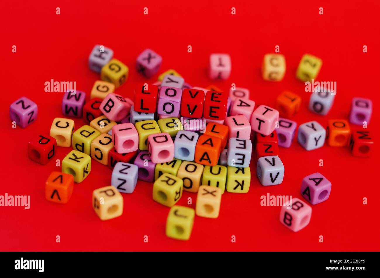Bunte Holzwürfelperlen mit Buchstaben auf rotem festlichem Hintergrund, Wort "Liebe". Valentinstag. 14 Februar. Flach liegend, Draufsicht. Stockfoto