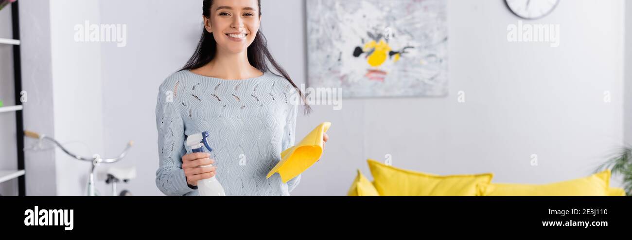 Fröhliche Frau Blick auf die Kamera, während sie Reinigungsmittel Spray und Lappen, Banner Stockfoto