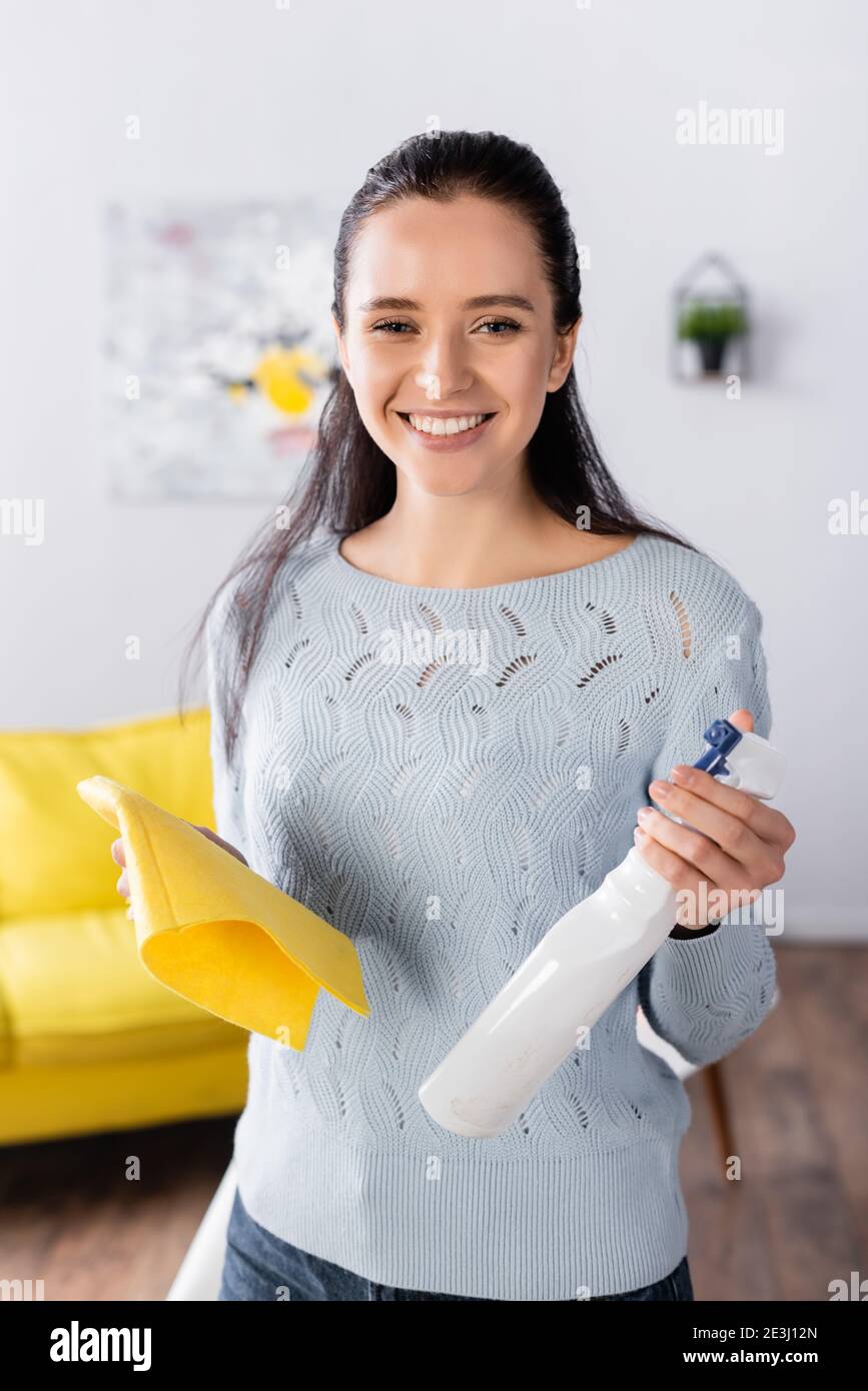 Junge Frau hält Waschmittel Spray und Lappen, während sie lächelt Kamera Stockfoto
