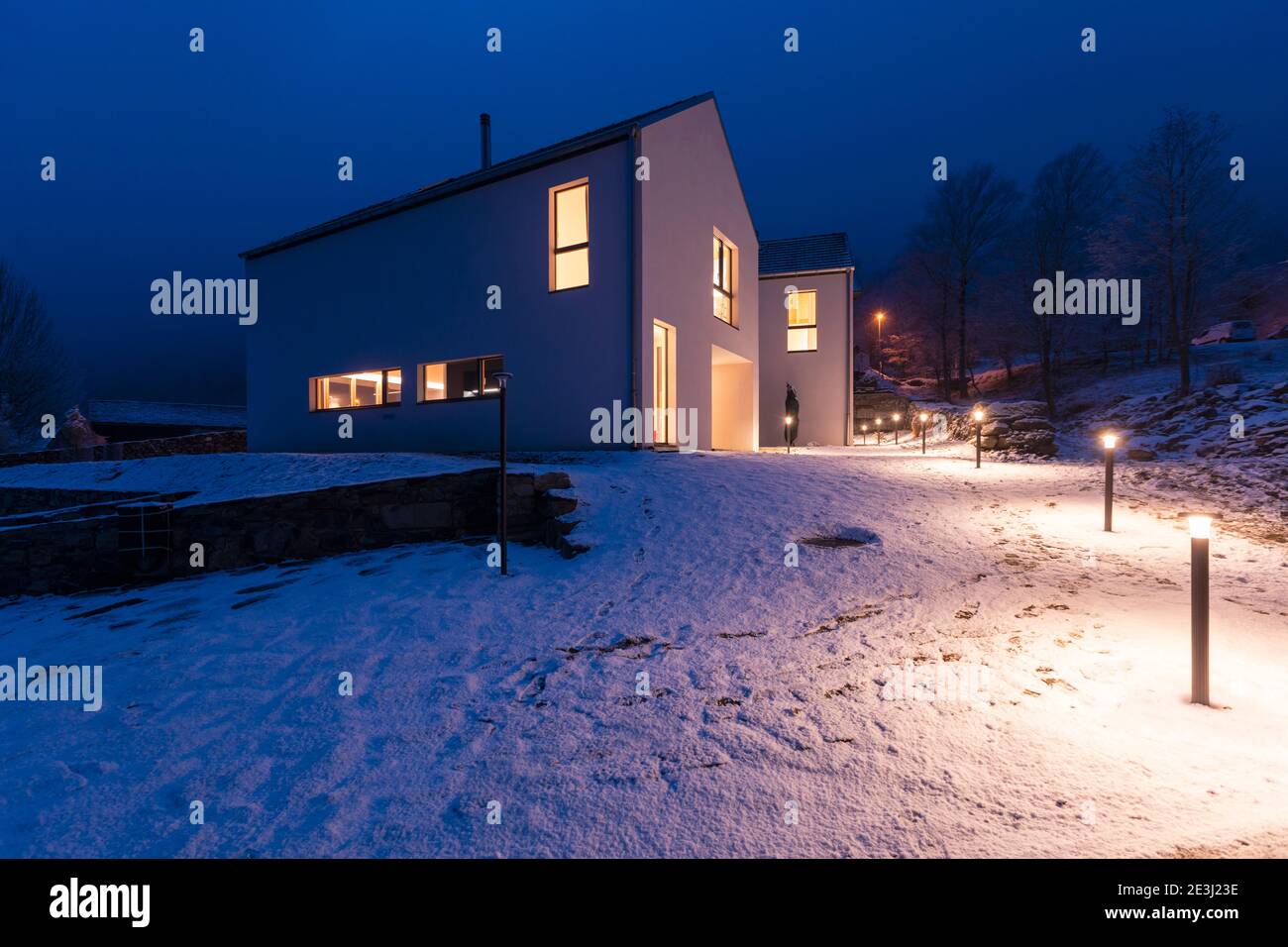 Modernes weißes Haus mit hellen Fenstern umgeben von Bergen, Schnee und Bäumen. Chirstmas Stimmung. Niemand drinnen. Stockfoto