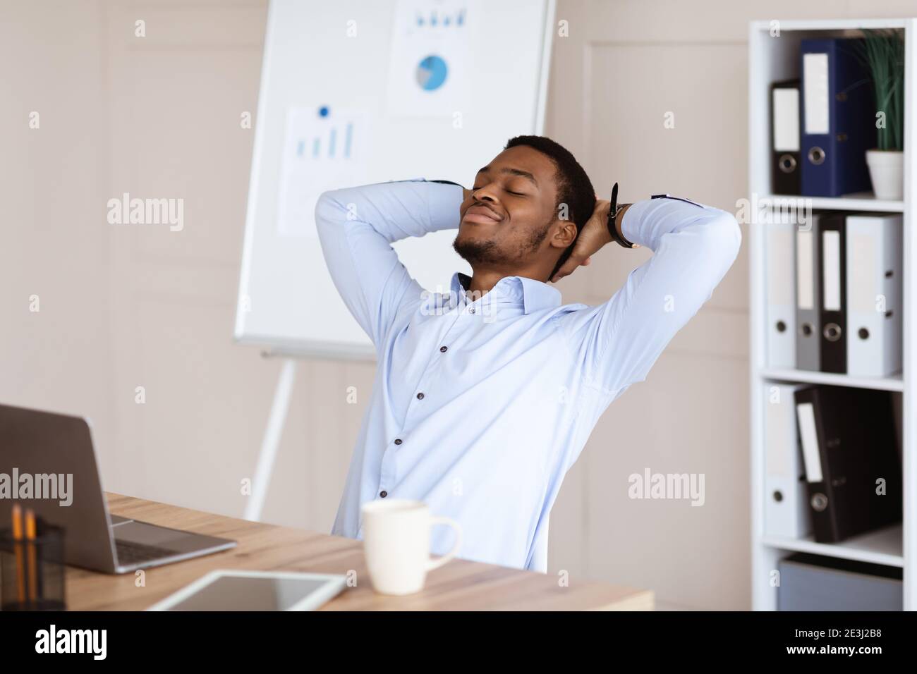 Fröhlicher afroamerikanischer Manager, der sich auf seinem Stuhl ausruhte Stockfoto