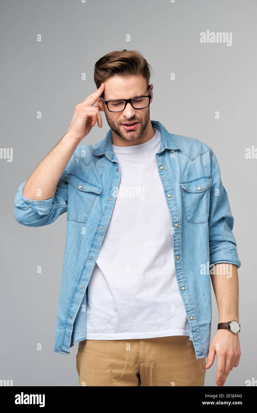 Frustriert junge kaukasischen Mann in Jeans Hemd berühren Kopf mit Hand im Stehen überg Studio grauen Hintergrund Stockfoto