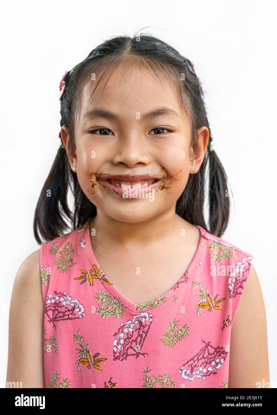 Portrait Asian niedlich Kind Mädchen mit chaotisch von Schokolade um den Mund, großes Lächeln auf niedlichen Gesicht, schwarze Haare, das Tragen schöner rosa Kleid, isoliert im Stockfoto