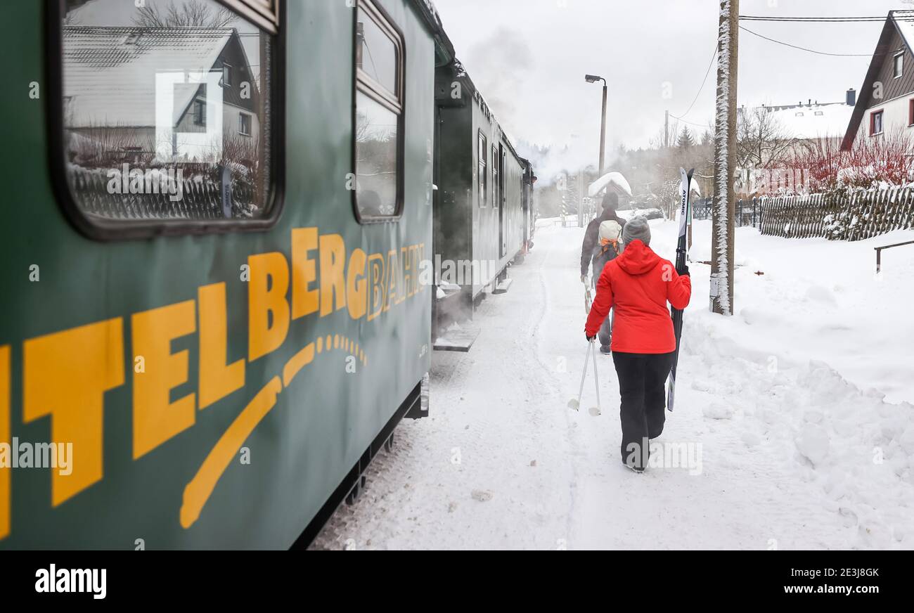 Sehmatal, Deutschland. Januar 2021. Zwei Wintersportler verlassen die Fichtelbergbahn in der verschneiten Station Kretscham-Rothensehma. Passagiere genießen derzeit einen herrlichen Blick auf die schneebedeckte Landschaft. Aber die Züge sind nur spärlich besetzt, genau wie die der anderen Bimmelbahnen in Sachsen. Aufgrund der Einschränkungen von Corona überschreiten die Züge, die hauptsächlich von Touristen genutzt werden, derzeit nicht die Kapazität von 25 Prozent. Quelle: Jan Woitas/dpa-Zentralbild/dpa/Alamy Live News Stockfoto