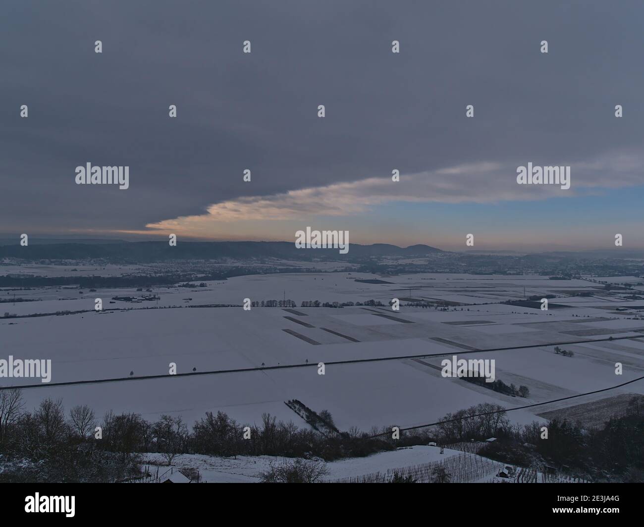 Schöne Luftaufnahme von Tal mit schneebedeckten landwirtschaftlichen Feldern in der Wintersaison mit Ausläufern der Schwäbischen Alb am Horizont unter aufhellenden Himmel. Stockfoto