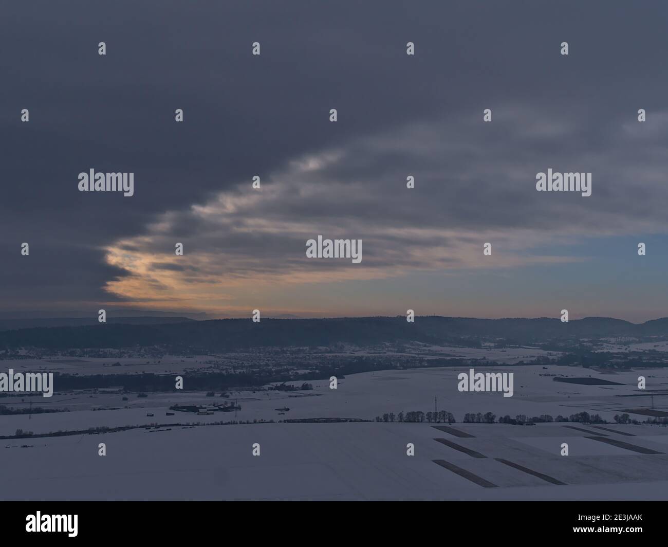 Schöne Luftpanorama des Tales mit schneebedeckten Feldern am Fuße der Schwäbischen Alb mit dramatischen Lichtung Himmel mit orangen Wolken. Stockfoto