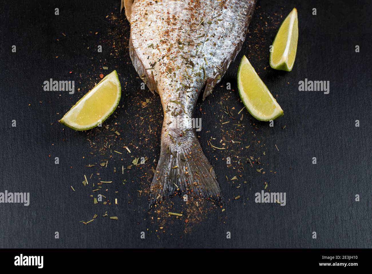 Schwanz aus frischem rohem dorado auf schwarzem Schiefersteinbrett mit Gewürzen, Kräutern, Zitrone und rotem Paprika. Brassen Fisch bereit zum Kochen. Draufsicht Stockfoto