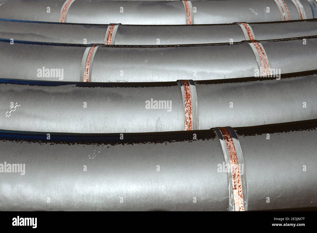 Schwarze Vergasungsrohre mit großem Durchmesser liegen an einem Sommertag in einer Reihe in einem offenen Lager auf der Straße. Stockfoto