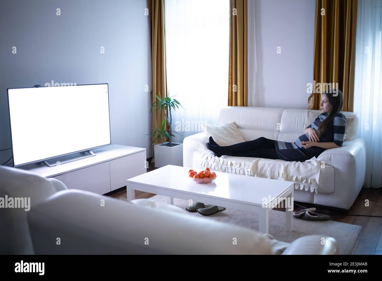Schöne schwangere Frau Fernsehen in ihrer modernen Wohnung Stockfoto