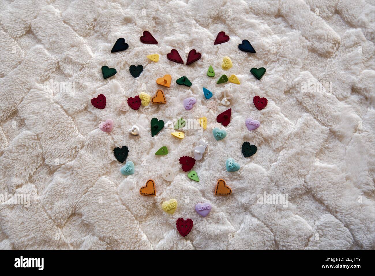 Mehrfarbiges Herzdesign auf einer weichen weißen Decke. Das Design besteht hauptsächlich aus herzförmigen Knöpfen. Stockfoto