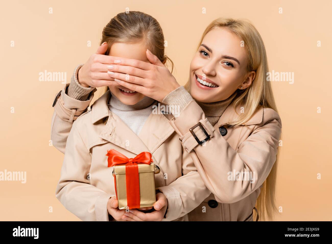 Glückliche Mutter, die Augen des Kindes mit Geschenkbox isoliert Auf Beige Stockfoto