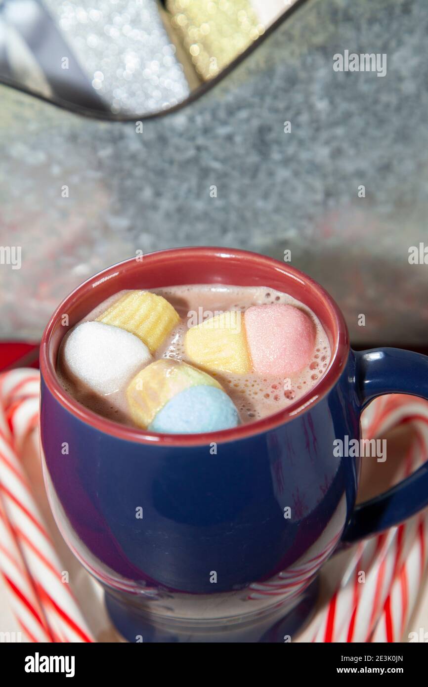 Blauer und roter Becher mit bunten Marshmallows auf einer Holzfläche mit Zuckerstöcken, neben einem Zinnhintergrund Stockfoto