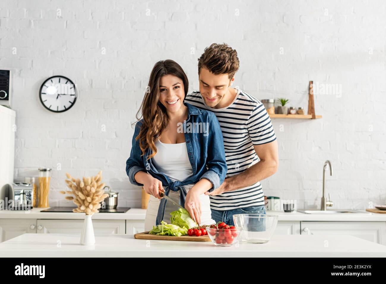 Fröhliches Paar bereitet Salat in der modernen Küche Stockfoto