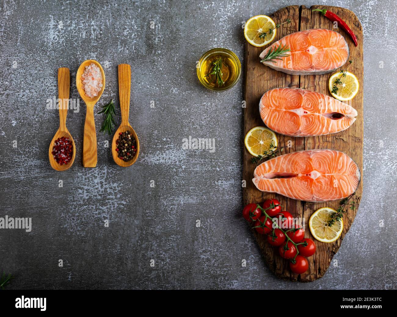 Drei rohe Steak Fischforelle, Lachs und Gewürze auf Holzbrett, dunkler Hintergrund Stockfoto