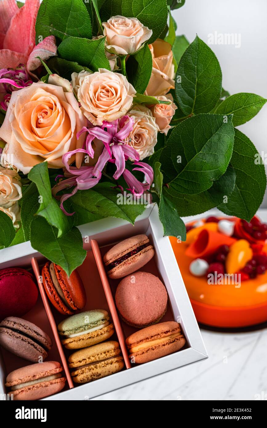 Geburtstagsgeschenk Blumen Blumenstrauß und Orange, Mango, Himbeerkuchen, bunte hausgemachte französische Macarons Stockfoto