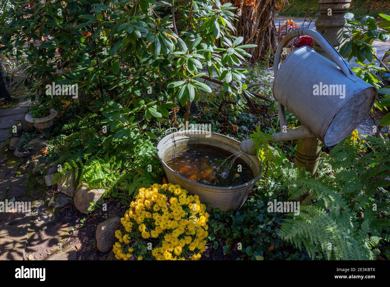 Gießkanne und Eimer aus Metall, die in einem Garten zu einem Wasserspiel gemacht werden. Stockfoto