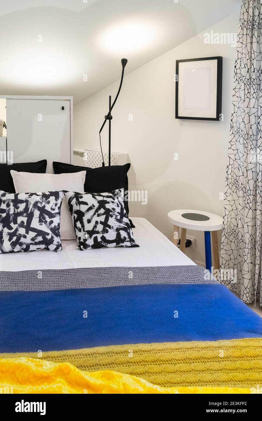 Das Innere eines kleinen neu eingerichteten Schlafzimmer im Dachgeschoss eines alten Hauses. Bett mit Kissen und Bettdecken in verschiedenen Farben Stockfoto