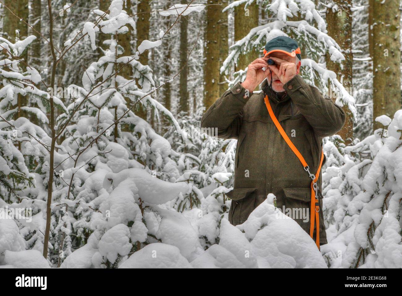 Ein Jäger steht im verschneiten Wald und beobachtet sein Jagdgebiet durch ein kleines Okular. Stockfoto