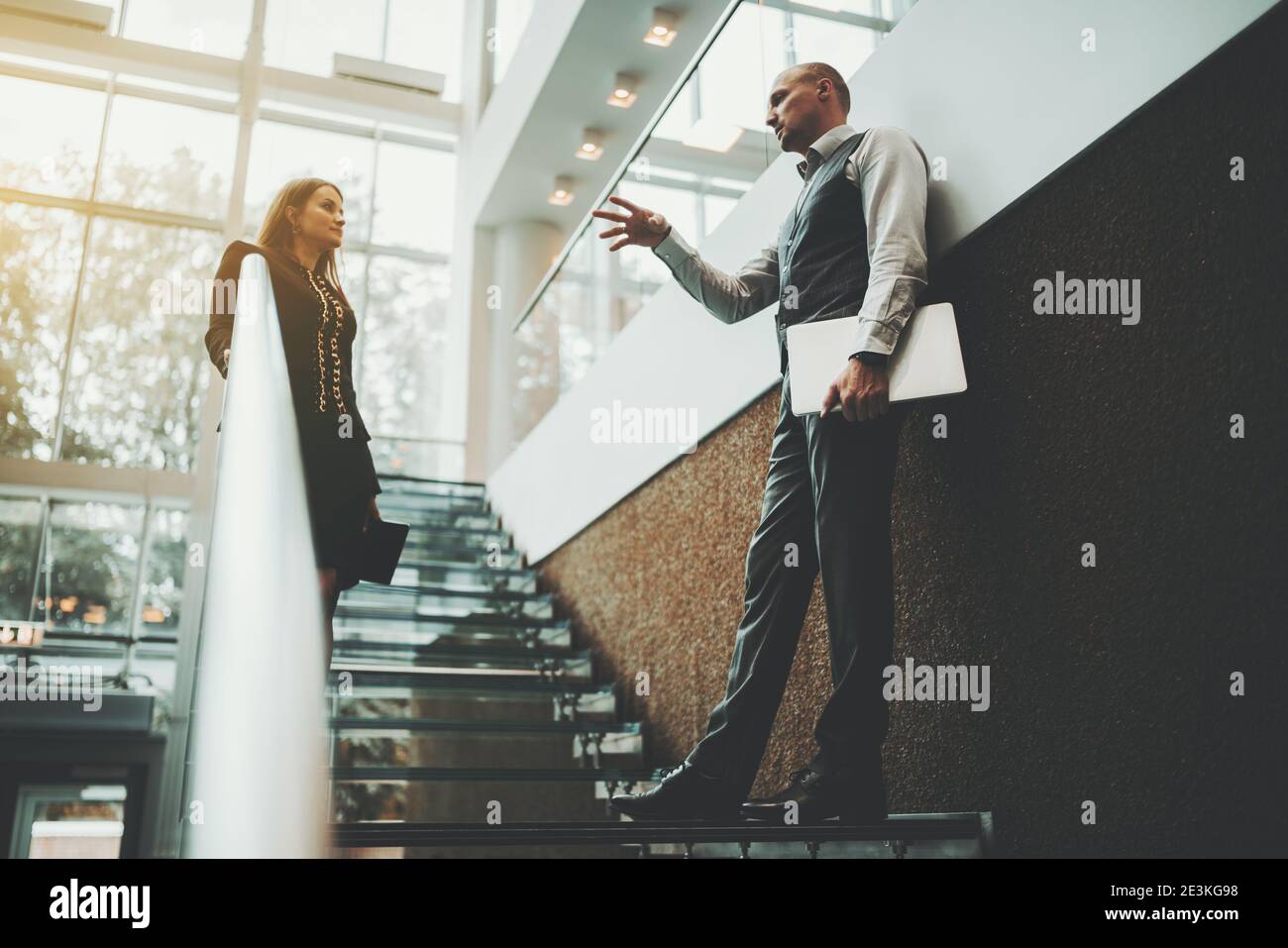 Eine Szene auf der Treppe eines modernen Luxusbüros Wolkenkratzer mit einem selektiven Fokus auf einen aktiv gestikulierenden Mann Unternehmer mit einem Laptop expliini Stockfoto